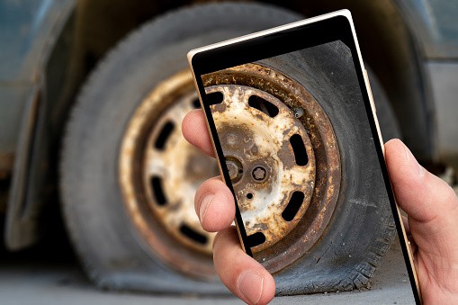 Old car wheel on smartphone screen. Car repair and disposal.